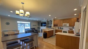 A modern kitchen with wooden cabinets, a central island with stools, and a dining area with a round table and chairs.