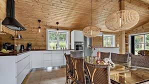 Une cuisine moderne avec des meubles blancs, une hotte noire et un coin repas comprenant des chaises en osier et une table avec un plateau en verre.