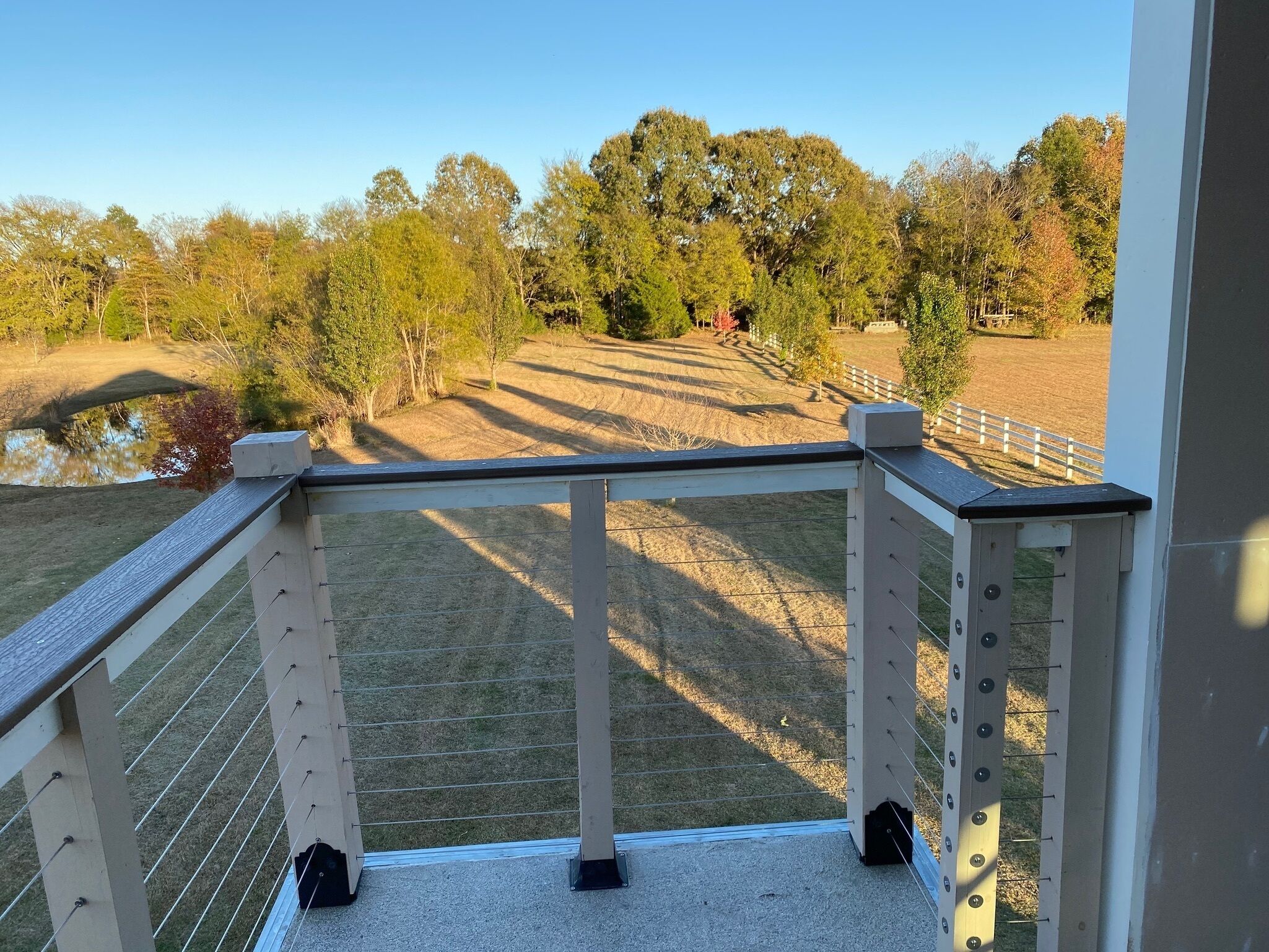 A balcony with a view of a fenced outdoor area, including a pond and trees.