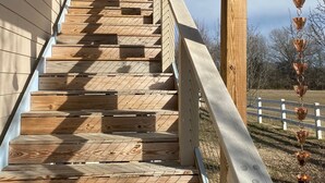A wooden staircase with metal railings leading to a covered area with a white fence in the background.