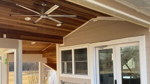 A covered patio area with a ceiling fan, wooden ceiling, and a bench.