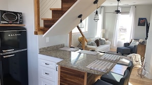 A kitchen with a Galanz refrigerator, wooden staircase, granite countertop, and a dining area with bar stools.