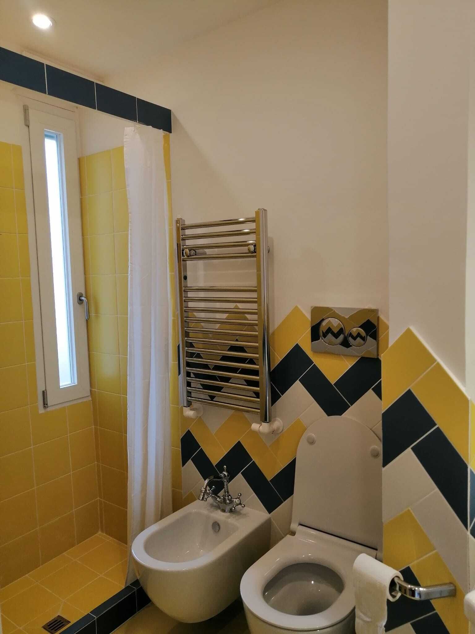 A bathroom with yellow and black tiles, a shower curtain, a towel rack, a bidet, and a toilet.