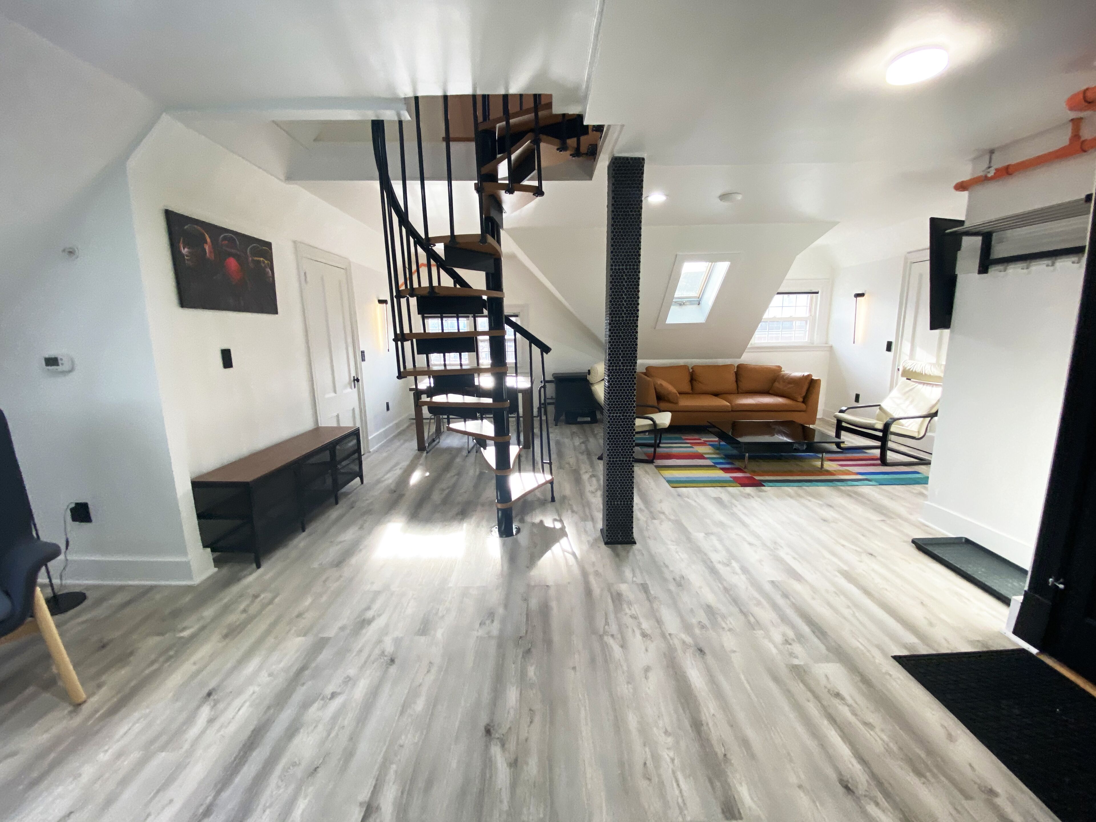 A spacious loft with a central staircase, a cozy seating area, and a large window providing natural light.