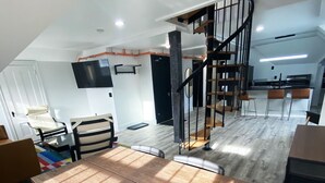 A modern interior with a dining area featuring a wooden table and chairs, a staircase with a metal railing, and a flat-screen TV mounted on the wall. - Victorian architecture dipped in refined modernity. May-June-July special!!! (Portland)