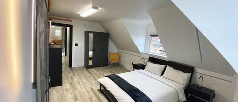 A bedroom with a sloped ceiling, a bed, a nightstand, a wardrobe, and a window.