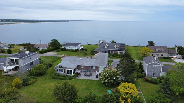 A residential area with houses near a body of water, featuring a mix of modern and traditional architecture, well-maintained lawns, and a clear view of the water. - Little Compton: Sweeping ocean view, 5min walk 2 beach, big yard w/ patio, 4 BRs (Little Compton)