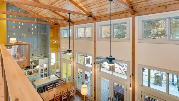 Un interior de varios niveles con vigas de madera, ventanas amplias y un comedor.