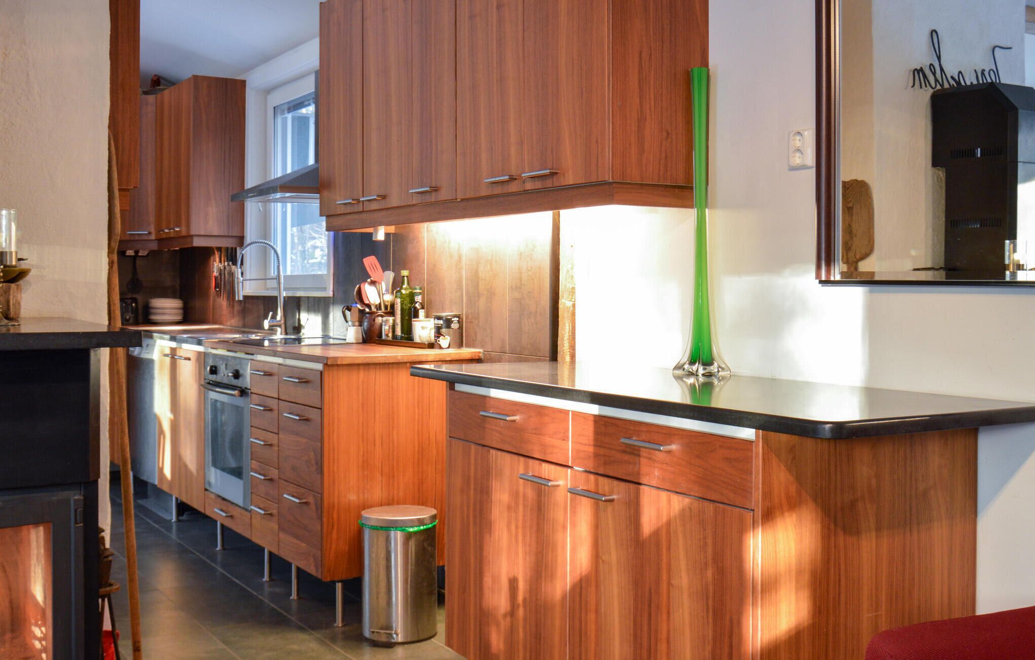 Una cucina moderna con mobili in legno, elettrodomestici in acciaio inossidabile e un vaso verde sul piano di lavoro.