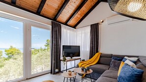 Ett modernt vardagsrum med ett stort fönster, en grå soffa, en tv och ett litet träbord.