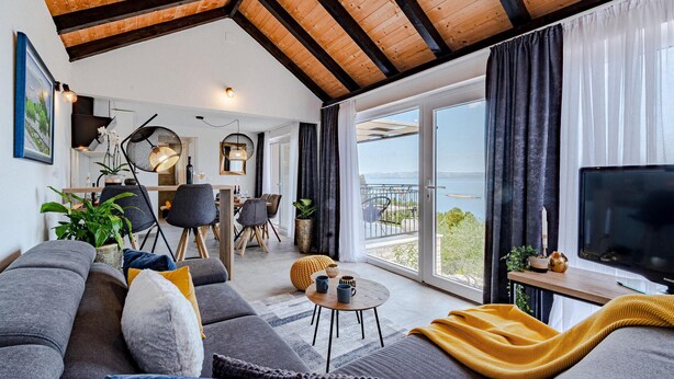 Ett modernt vardagsrum med en soffa, ett soffbord och en tv. Det finns en balkong med utsikt över havet.