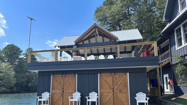 A waterfront house with a wooden deck, two large sliding doors, and white Adirondack chairs. - Lake Rabun Rental - Classic Waterside Home and Boathouse (Lakemont)