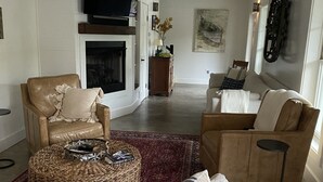 A spacious living room with a large sofa, a smaller armchair, a coffee table, and a fireplace. - Lake Rabun Rental - Classic Waterside Home and Boathouse (Lakemont)