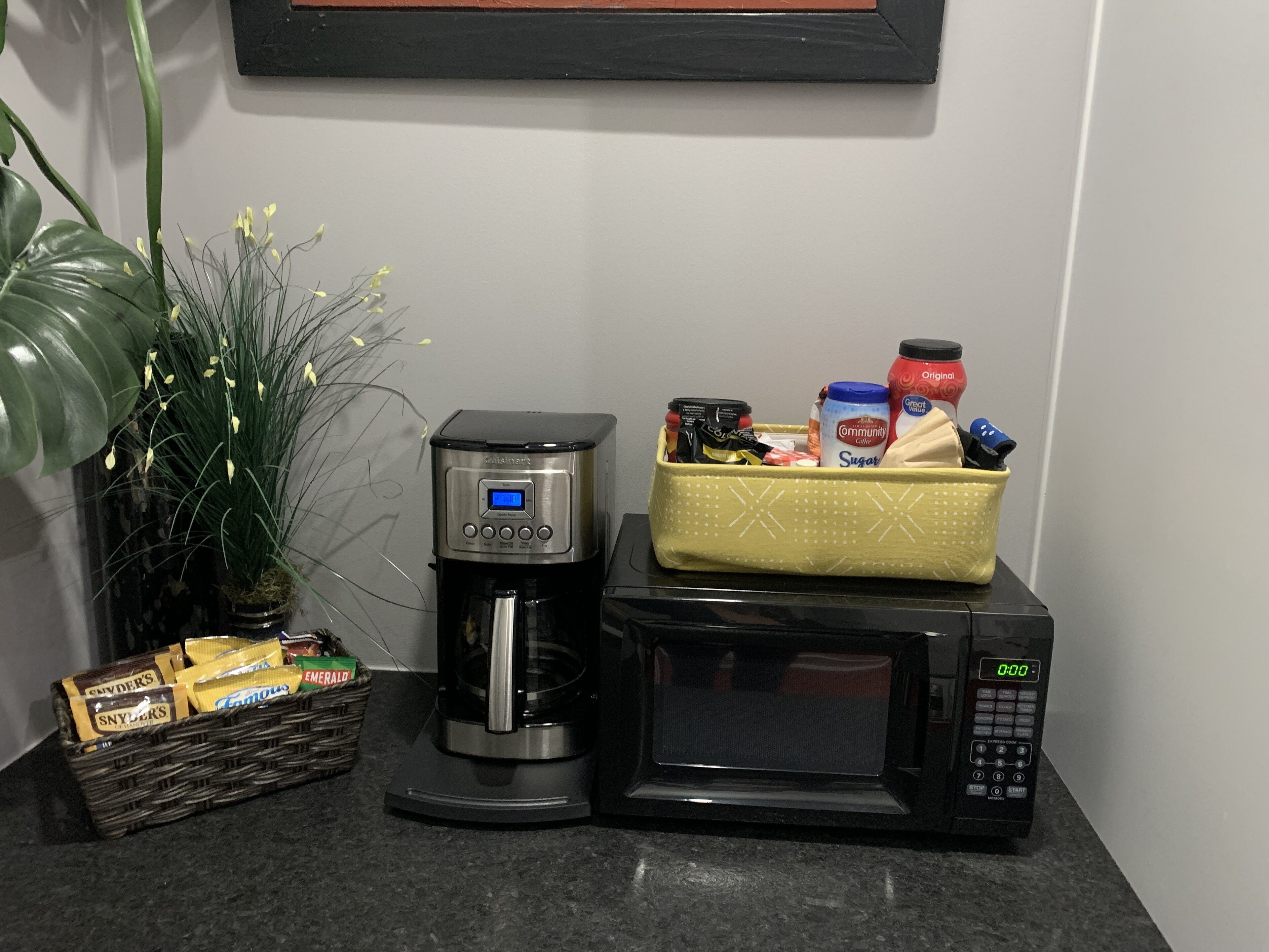 Een kitchenette met een koffiezetapparaat, magnetron en een mand met lekkernijen.