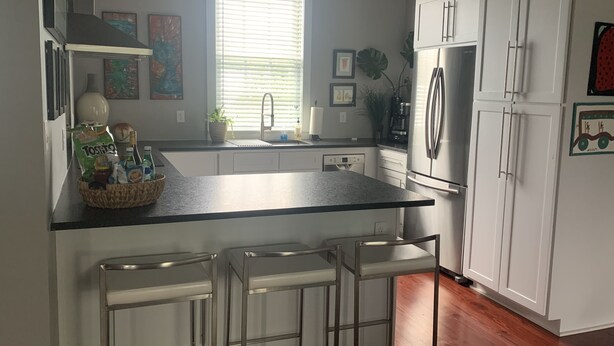 A modern kitchen with white cabinets, a stainless steel refrigerator, and a window with blinds.