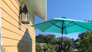 A wooden deck with a green umbrella, a chair, and a potted plant.