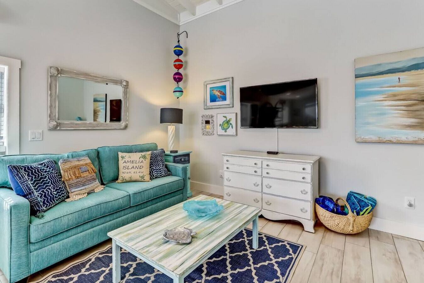 A living room with a teal sofa, a coffee table, a white dresser, and a TV.