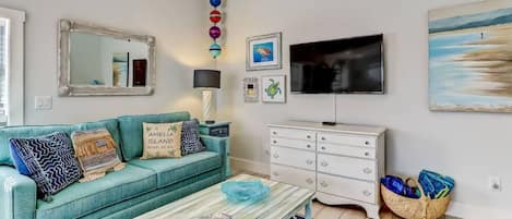 A living room with a teal sofa, a coffee table, a white dresser, and a TV.