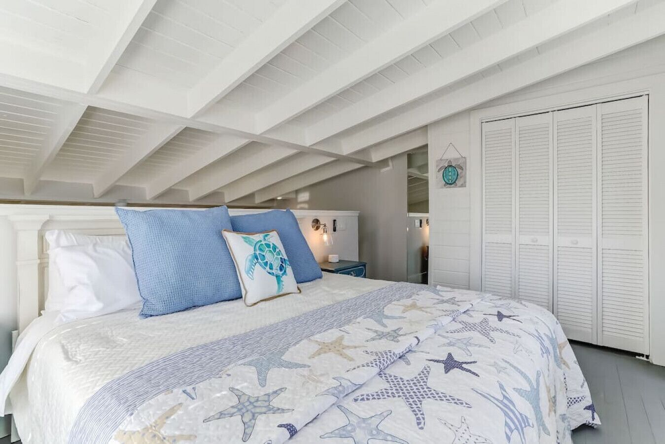 A bedroom with a bed, white headboard, and a ceiling with exposed beams.