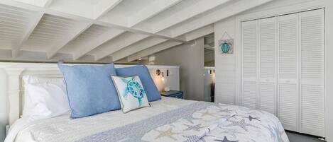 A bedroom with a bed, white headboard, and a ceiling with exposed beams.