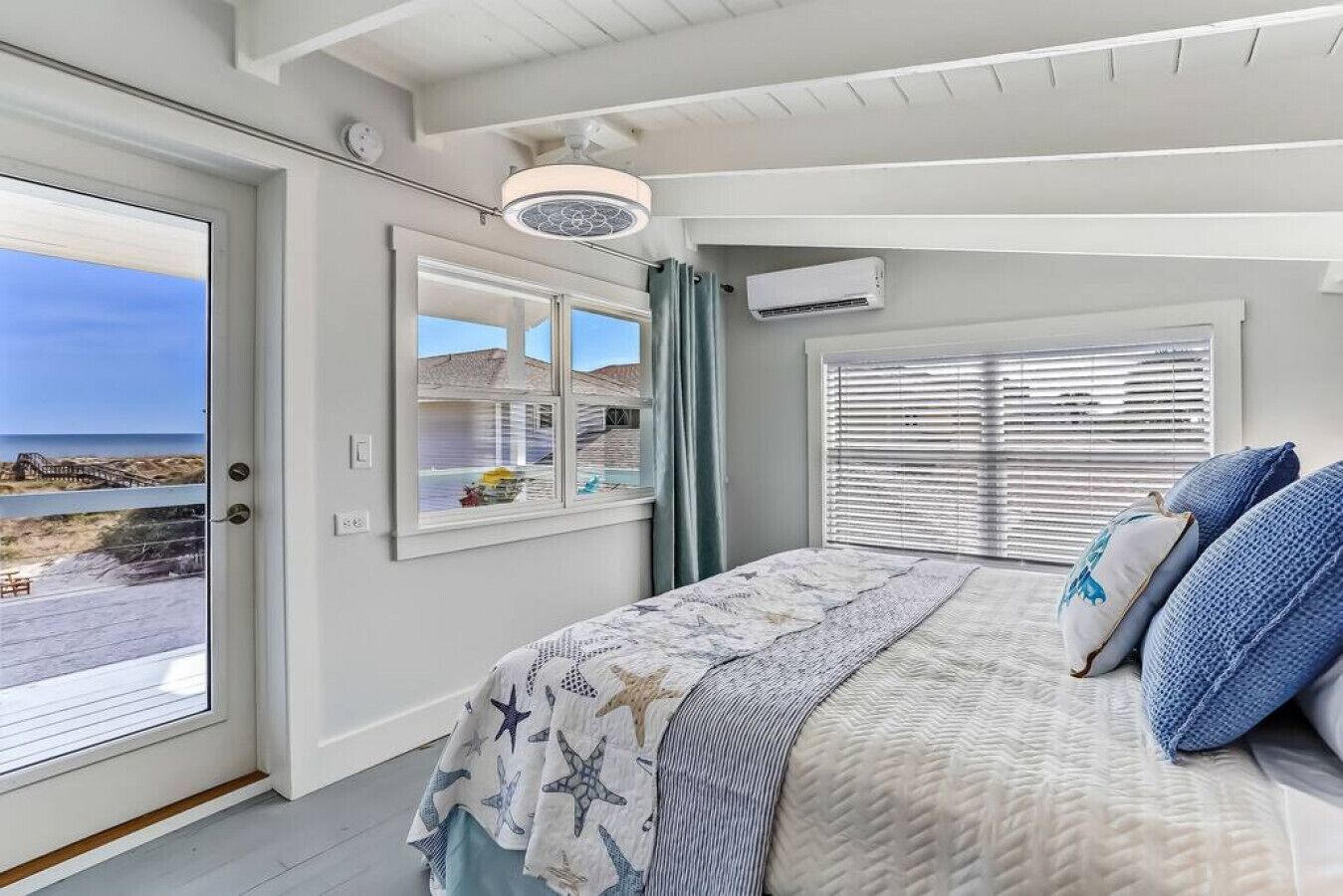 A bedroom with a large bed, a view of the beach, and a ceiling fan.