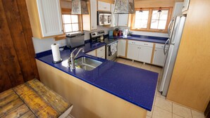 Une cuisine dotée d’un plan de travail bleu, d’appareils électroménagers en acier inoxydable, de meubles en bois et de luminaires suspendus.