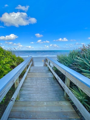 Un paseo marítimo de madera que conduce a una playa con cielos despejados y vistas al océano.