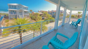 Ein Balkon mit türkisfarbenen Stühlen, Blick auf einen Strand und ein zweistöckiges Haus im Hintergrund.
