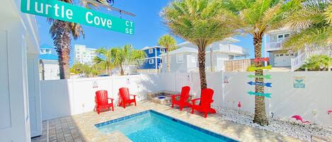 Une piscine avec des chaises rouges, un panneau indiquant « Turtle Cove », et des palmiers.