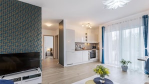 Een moderne woonkamer met een flatscreen televisie, een salontafel met een vaas, en een eethoek met een tafel en stoelen.