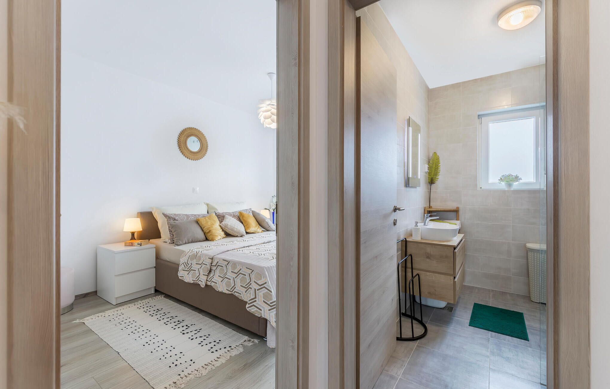 Una camera da letto con un letto, comodini e una lampada da comodino. C'è un bagno con un lavandino, uno specchio e una finestra.