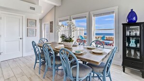 Un comedor con una mesa de madera, sillas azules y vista al océano.