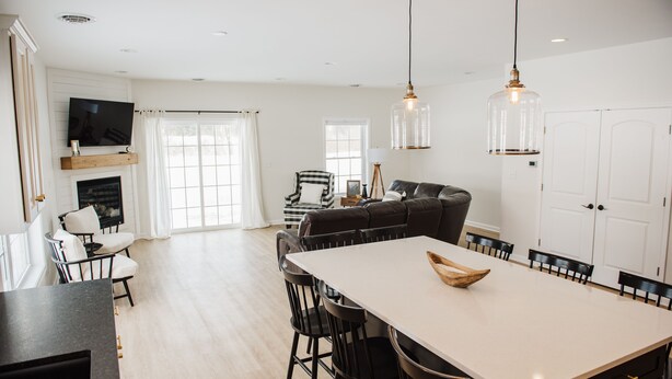 A spacious living area with a large dining table, black chairs, a sofa, and a television mounted on the wall.