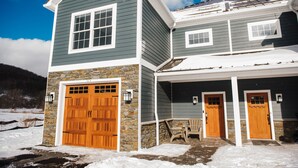 A two-story house with a stone foundation, a large wooden garage door, and a covered porch with two doors.