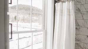 A bathroom with a large window, a shower curtain, and marble tiles.