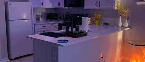 A modern kitchen with white cabinets, a central island, a microwave, and a stove.