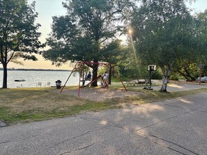 Un parque con un columpio, mesas de picnic y una canasta de baloncesto.