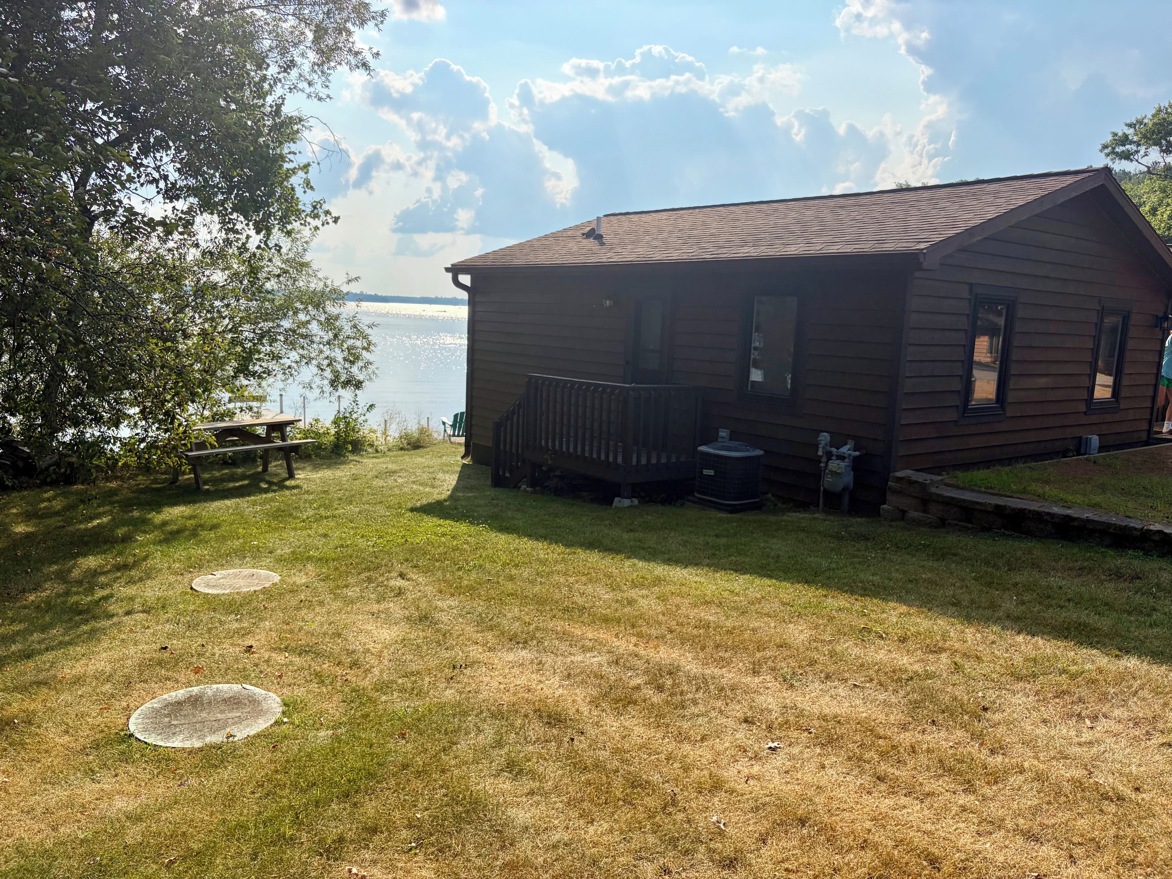A cabin with a deck, a picnic table, and a view of a body of water.