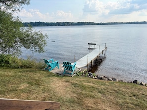 A lakeside dock with two chairs and a bench, surrounded by grass and trees.