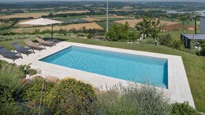 A rectangular swimming pool with lounge chairs and a view of a rural landscape.