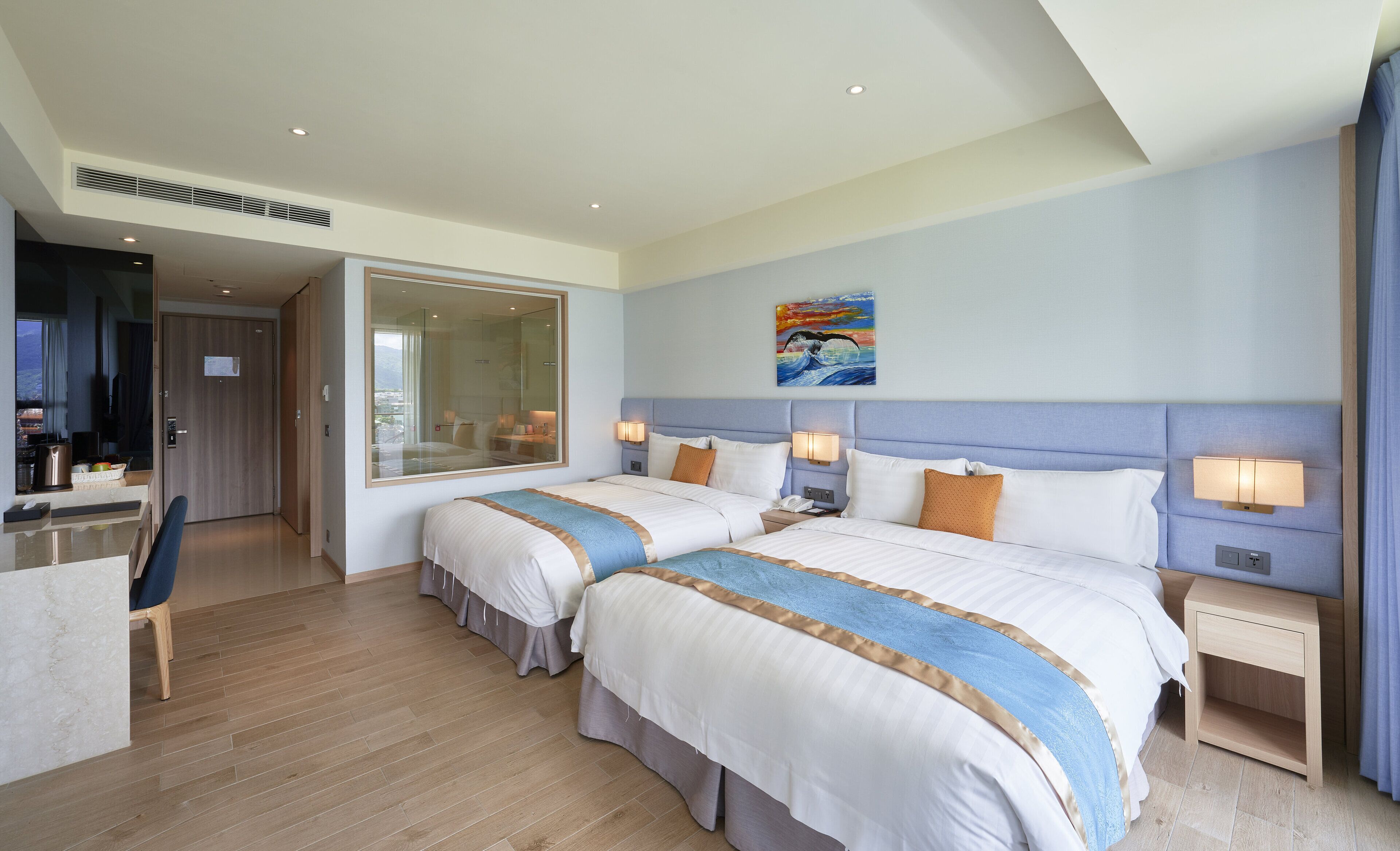 A hotel room with two beds, a desk, and a large window.