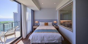 Habitación de hotel con una cama grande, dos mesitas de noche con lámparas, y vistas al mar desde un balcón, además de un box de ducha de vidrio.
