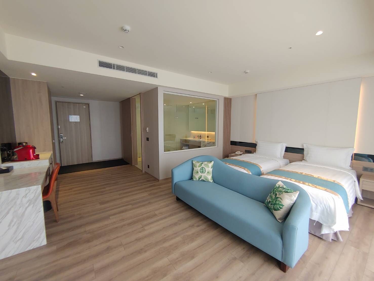A hotel room with a bed, a sofa, a desk, and a mirror.