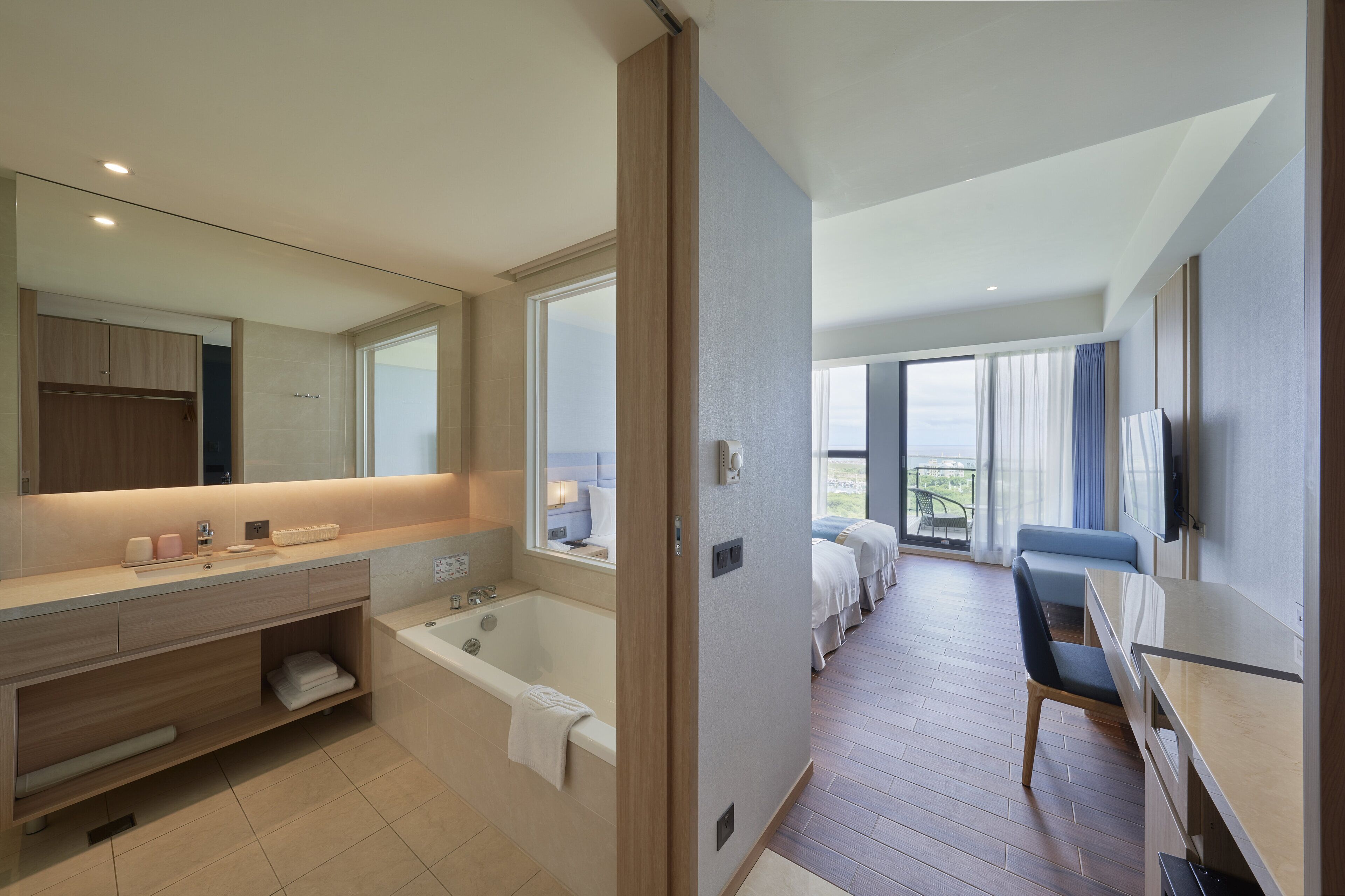 A modern hotel room with a large bathroom, a balcony with a view, and a desk with a chair.