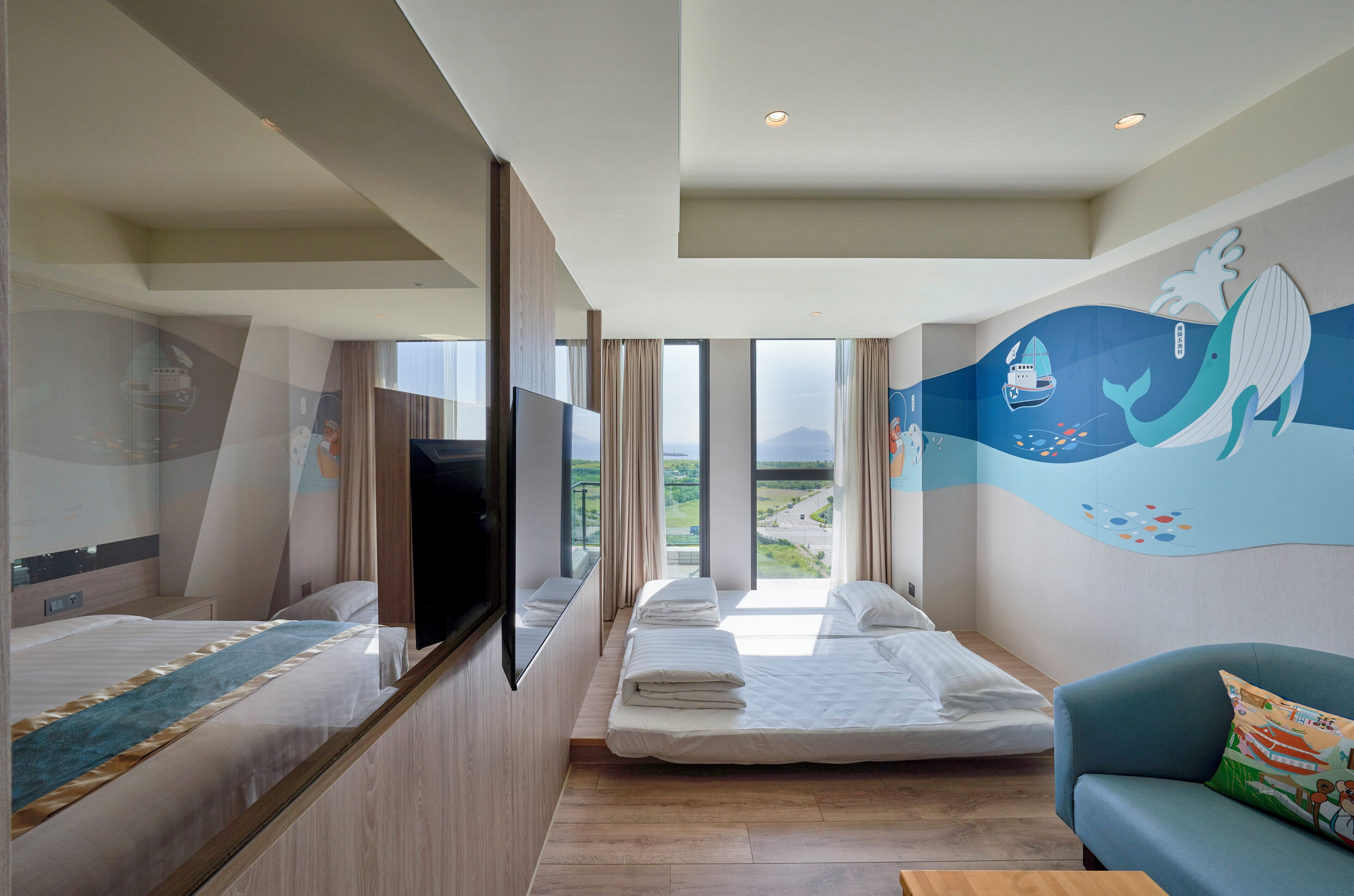 A hotel room with two beds, a TV, a large window with a view, and a mural on the wall.