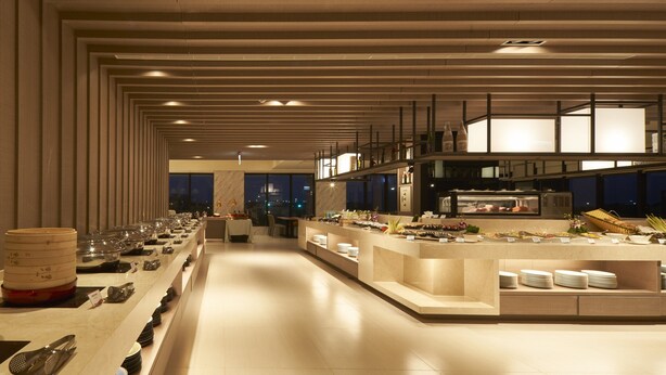A modern hotel dining area with a long buffet line, a kitchen area, and a view of the city at night. - Lan Yang Seaview Hotel (Toucheng)