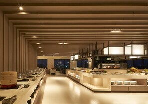 A modern hotel dining area with a long buffet line, a kitchen area, and a view of the city at night. - Lan Yang Seaview Hotel (Toucheng)