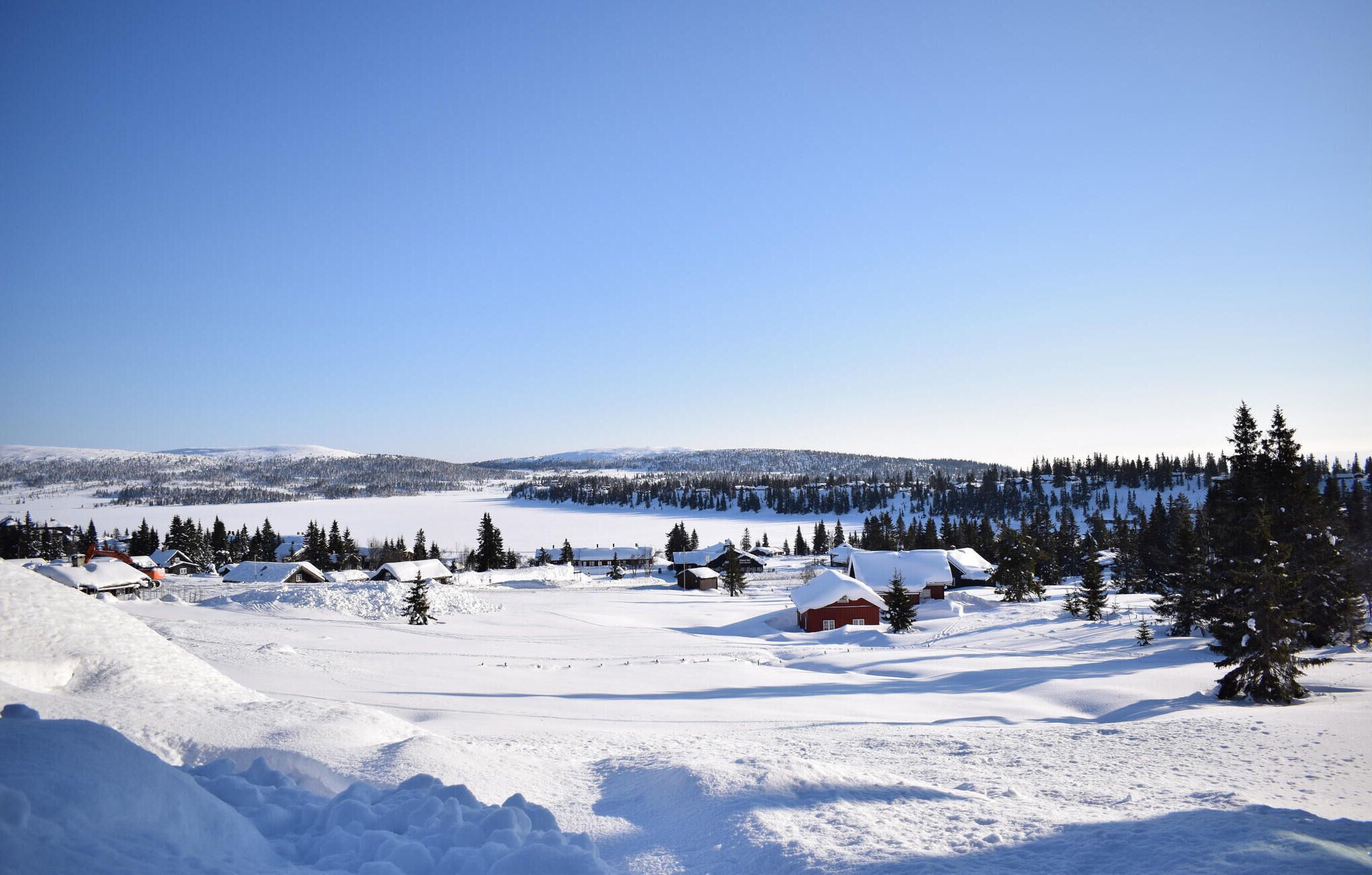 Schneebedeckte Landschaft mit einer Gruppe von Hütten und einem See im Hintergrund.