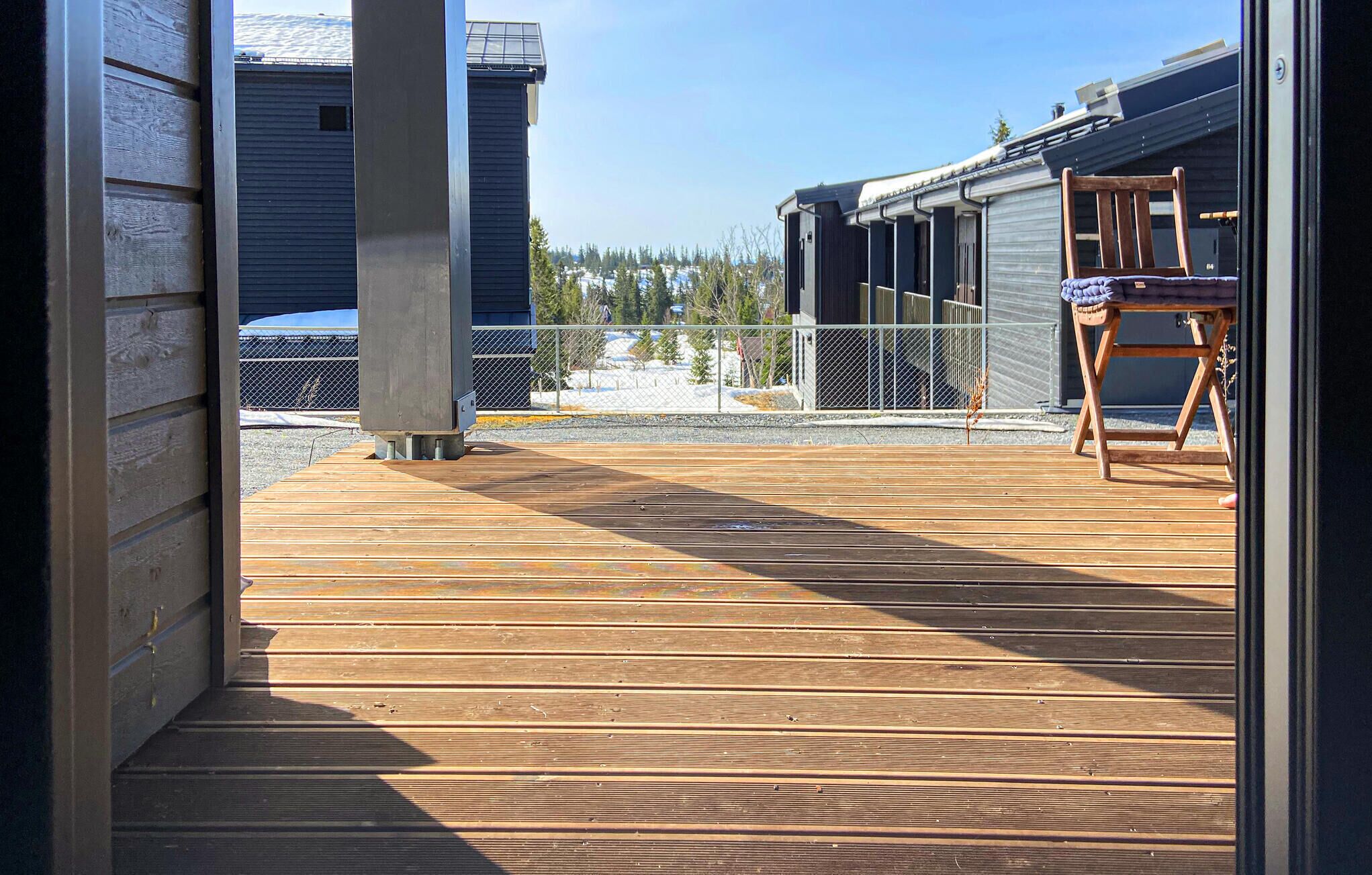 A wooden deck with a metal railing, a chair, and a building in the background.