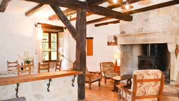 Un intérieur rustique avec des poutres apparentes, une cheminée en pierre et un coin repas agrémenté de meubles en bois.